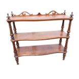 A Victorian walnut whatnot of serpentine outline having three shelves and scroll carved pierced