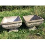 A pair of square composition stone urns with moulded rims above floral embossed friezes, raised on
