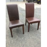 A pair of modern leather side chairs with high backs and padded tapering seats, raised on square