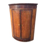 An early C19th oak barrel fronted corner cupboard with moulded cornice above an inlaid frieze, the