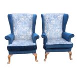 A pair of velour upholstered wingback armchairs with flared arms above loose cushions on sprung