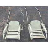 A pair of painted swinging childs chairs with rounded backs and slatted seats, the arms supported by