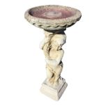 A composition stone birdbath with circular bowl supported by a draped cherub holding a cornucopia