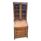 A 1930s carved oak bureau bookcase, the top with leaded glass doors beneath a floral pressed band,