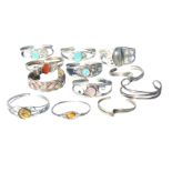 Twelve contemporary silver bangles, mostly mounted with polished semi-precious stones, plaited,
