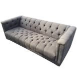 A contemporary rectangular button upholstered sofa in grey linen with brass studding, raised on