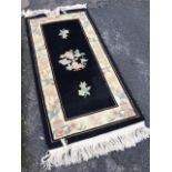 A Chinese thick pile wool rug woven with floral sprigs on black field framed by ivory border with
