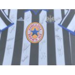 A framed Newcastle United shirt, signed by team members. (30.75in x 32.75in)