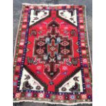 An Iranian rug woven with central hooked floral medallion on red field with camels and