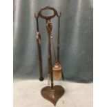 A set of wrought iron fire tools, the stand on heart shaped base with column holding tongs,