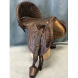 A leather western style saddle with decorative scrolled stitching and detachable arched back, hung
