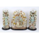 A trio of Edwardian glass domes containing decorative figure groups among silk flowers