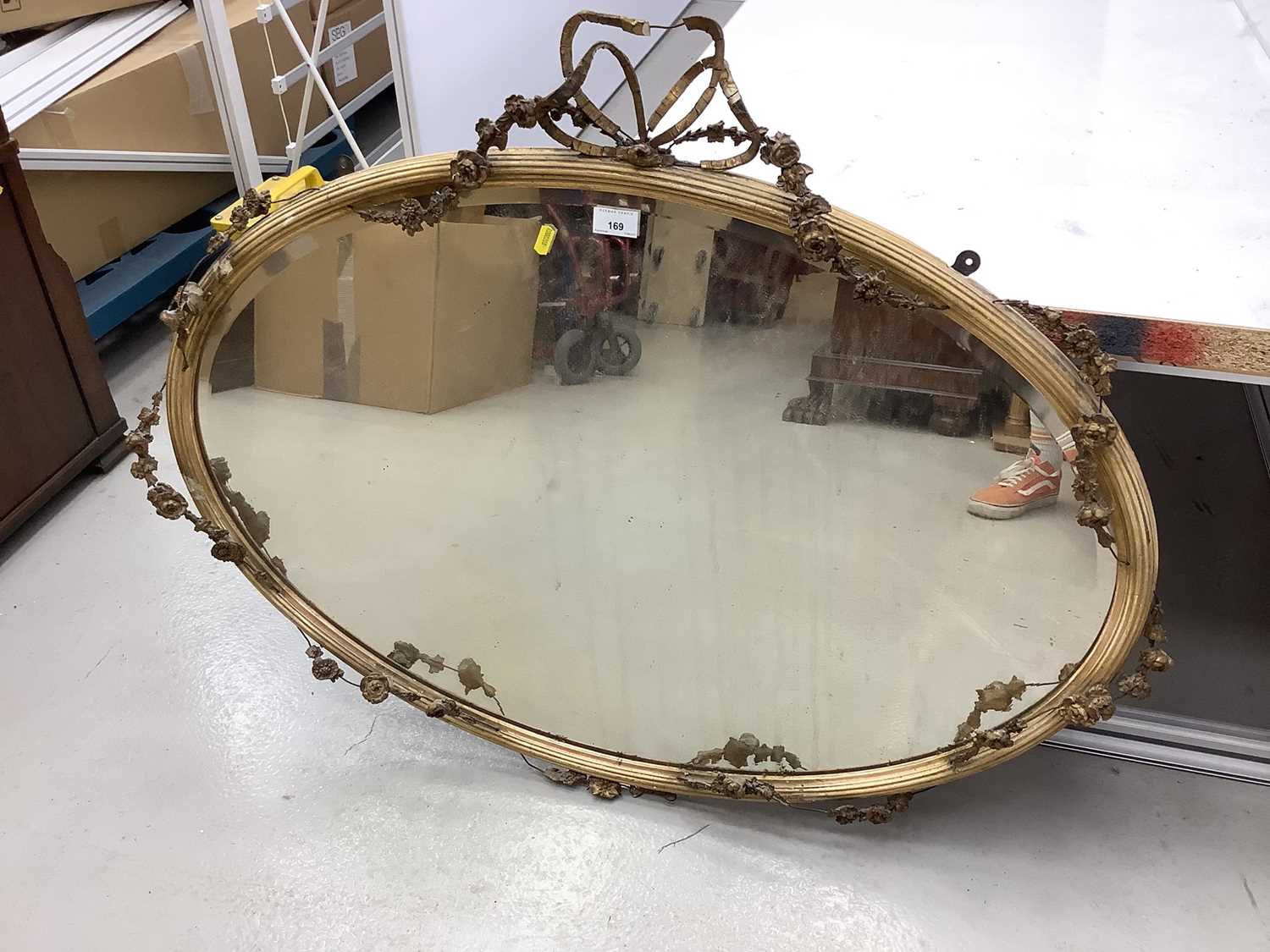 Oval wall mirror in ornate gilt frame with ribbon and swag decoration, 100cm x 77cm