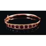 Late Victorian ruby and diamond hinged bangle with nine graduated oval mixed cut rubies interspaced