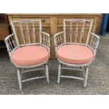 Pair of painted open elbow chairs with decorative shaped backs, caned seats with cushions, on shaped