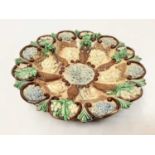 Castle Hedingham Edward Bingham pottery dish decorated with masks and flowers on brown and green gro