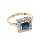 Sapphire and diamond cluster ring with a square step cut blue sapphire surrounded by a border of sin