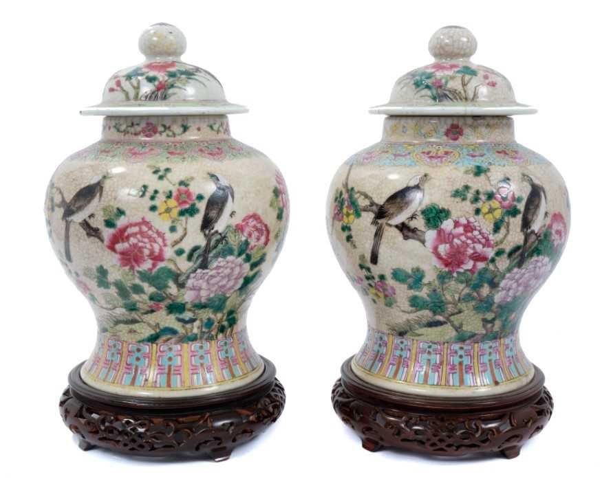 Pair of Chinese famille rose porcelain crackle-glazed jars and covers with carved hardwood stands, a