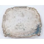 George V silver salver of shaped square form with piecrust border, on four leaf scroll feet