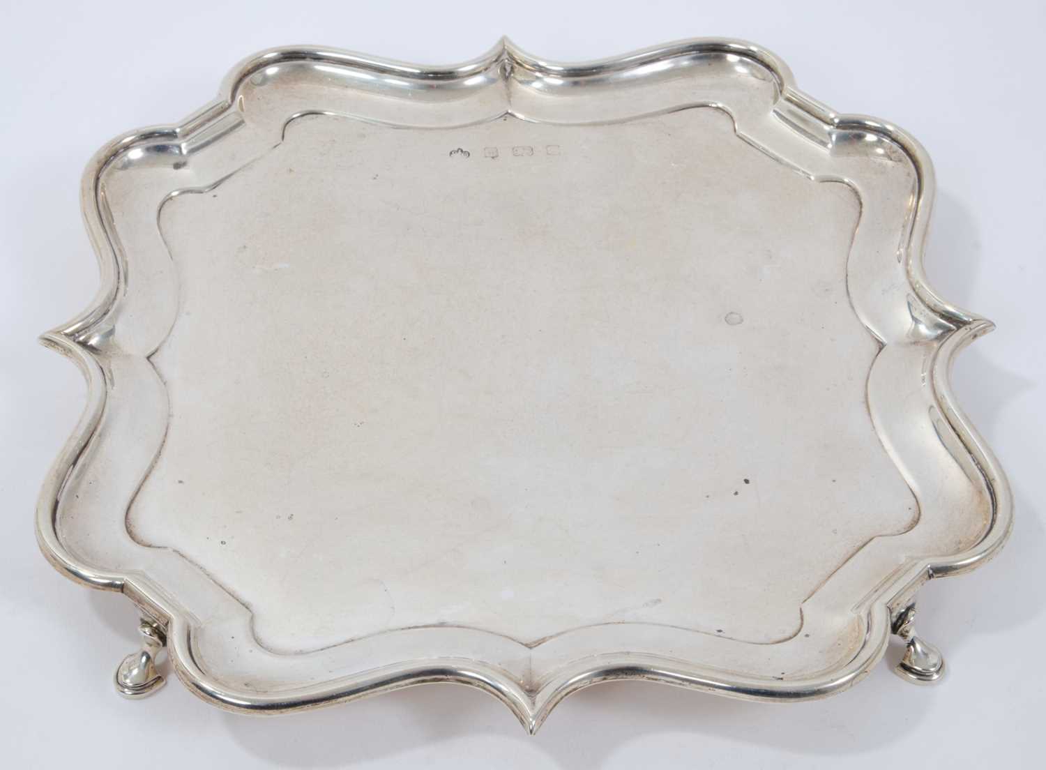 Early George V silver salver of shaped square form, with piecrust border, on four hoof feet