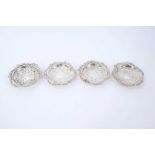 Set of four 1930s silver dishes of circular form, with raised scroll and floral borders