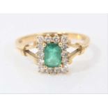 Emerald and diamond cluster ring with a rectangular step cut emerald surrounded by a border fourteen