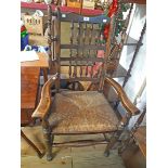 A 20th Century stained elm framed high spindle back wing elbow chair with wide woven rush seat