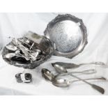 A silver plated cake basket containing a quantity of assorted cutlery, including two basting
