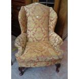 A late 19th Century wingback armchair in the Georgian style with remains of upholstery, set on