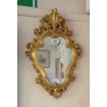 A small Rococo style gilt plaster framed wall mirror with shaped plate