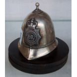 A small plated metal Metropolitan Police helmet deskweight with circular base