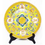 An antique Chinese porcelain yellow ground plate decorated with four character symbols, trailing