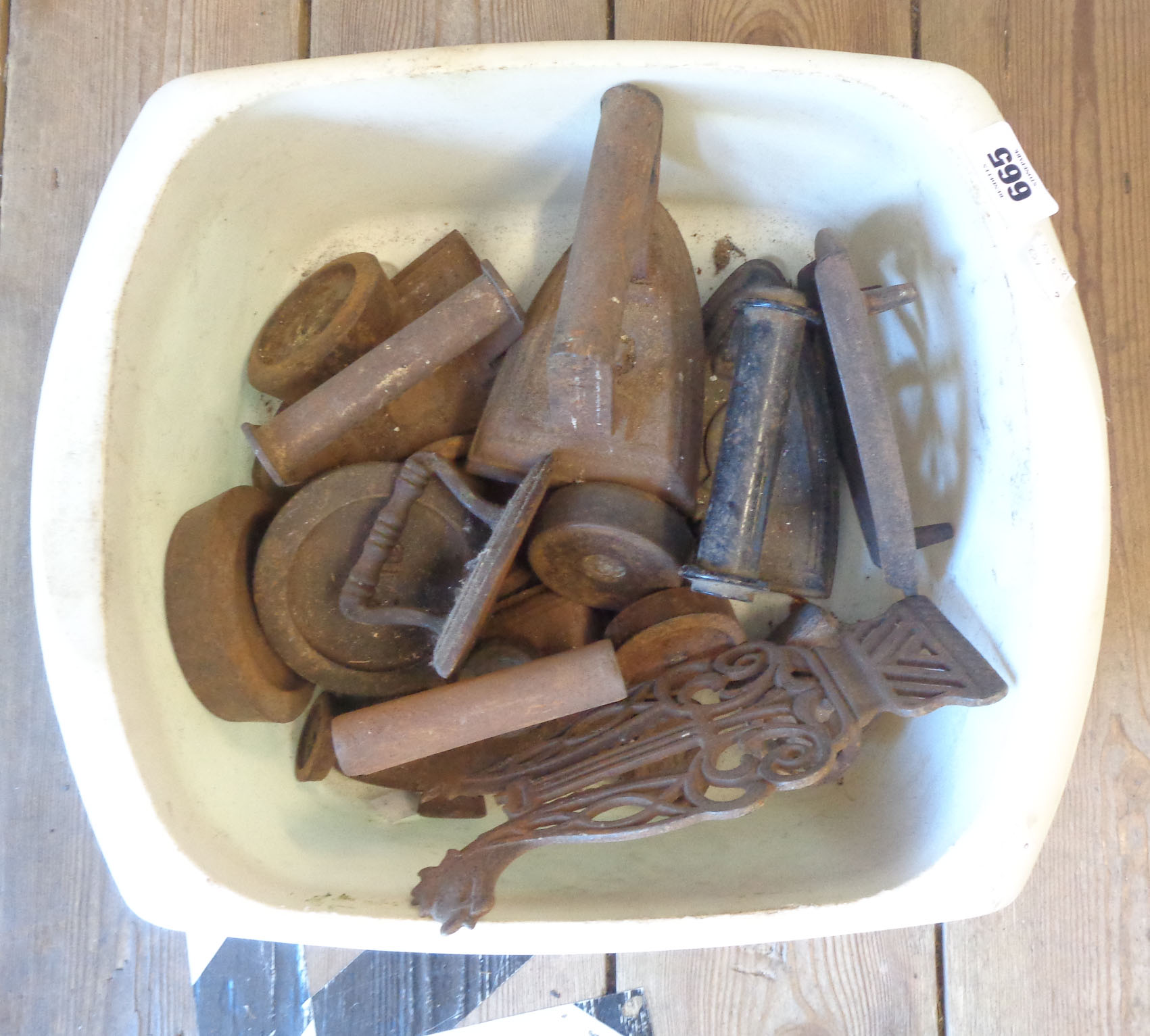 A bowl containing a selection of old flat irons including miniature, weights, etc.