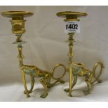 A pair of cast brass chamber candlesticks in the form of candle holders being held aloft by devilish
