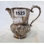 An early 20th Century silver ornate cream jug with cast scroll handle, hammered, incised and