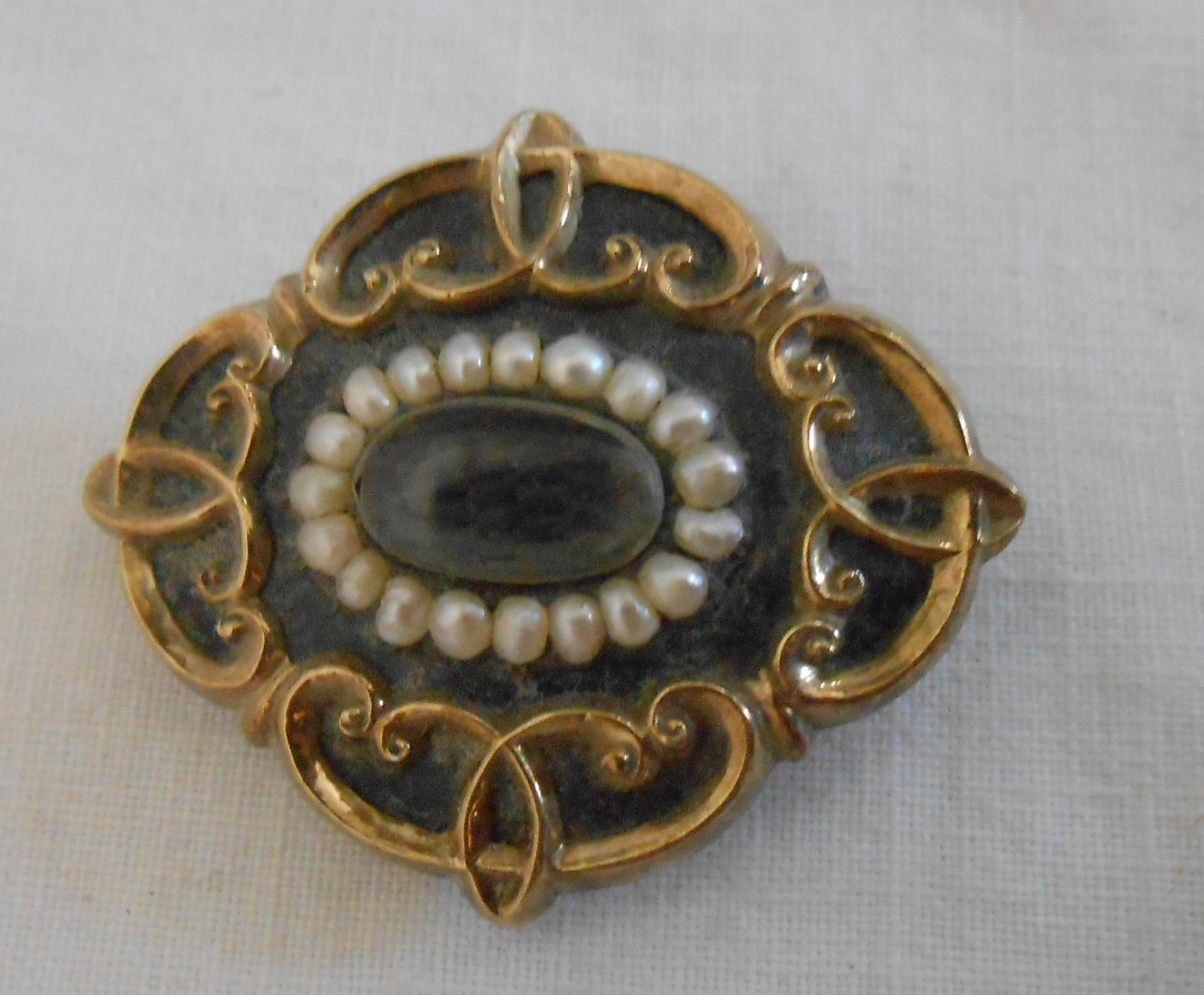 A Victorian yellow metal mourning brooch with central hair panel within a seed pearl border, on