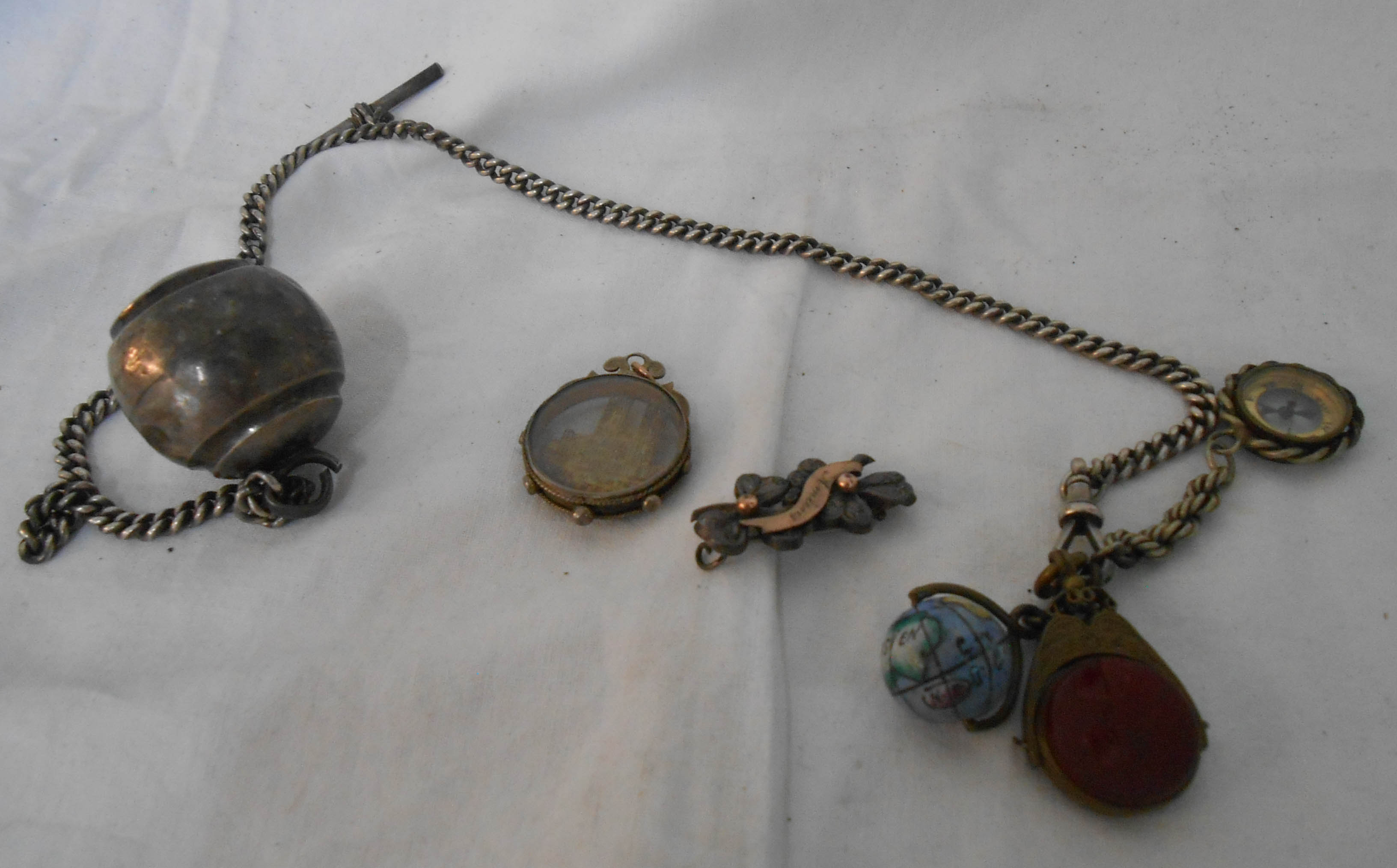 A silver watch chain with silver bell, enamelled globe of the world, compass and other fobs