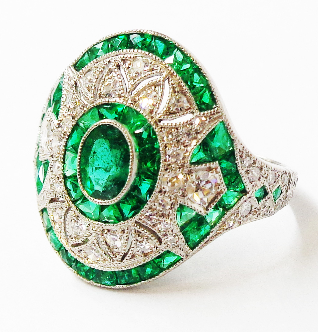 A marked PLAT Art Deco style curved panel ring, set with various cut emeralds and diamonds in a