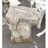 A concrete garden statue depicting a troll with a book on his head