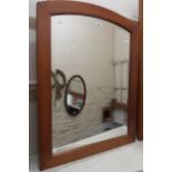 A modern stained wood framed wall mirror with curved top to bevelled plate