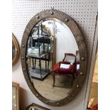 An early 20th Century decorative brass clad framed bevelled oval wall mirror with riveted strap work