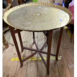 A 60cm diameter old brass tray top table with petal border and repeat design, set on a folding base