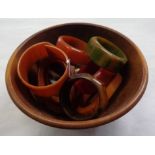 A small turned wood bowl containing a quantity of Art Deco phenolic napkin rings in various colours,
