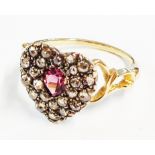 An unmarked yellow metal ring with pink stone to centre of old cut diamond encrusted heart shaped