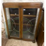 A 92cm polished oak display cabinet with glass shelves enclosed by a pair of Art Deco leaded