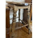 An antique oak stool with pierced handle to top, set on turned supports