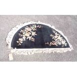 A semi circle shaped machine made rug with florals motifs on black ground