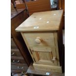 A modern pine bedside cabinet with short drawer, enclosed by a panelled door