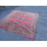 A large Middle Eastern handmade rug with ornate green decoration and blue highlighting on red ground