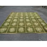 A large handmade olive green rug with repeating flower motifs within square panels - 2.9m X 2.9m